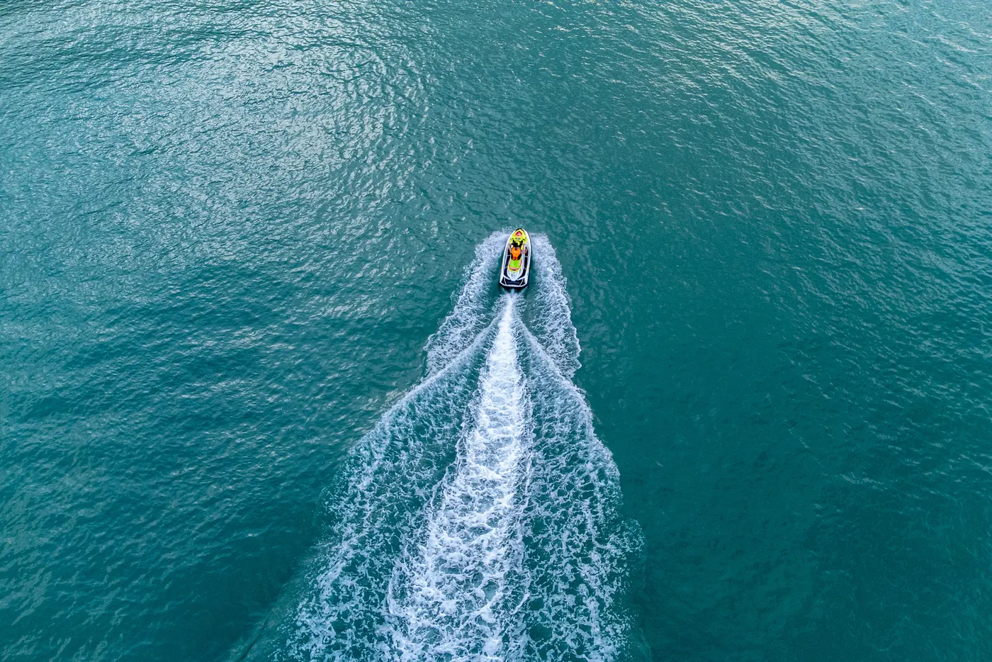 A jet ski leaving a white wake across turquoise water, seen from above