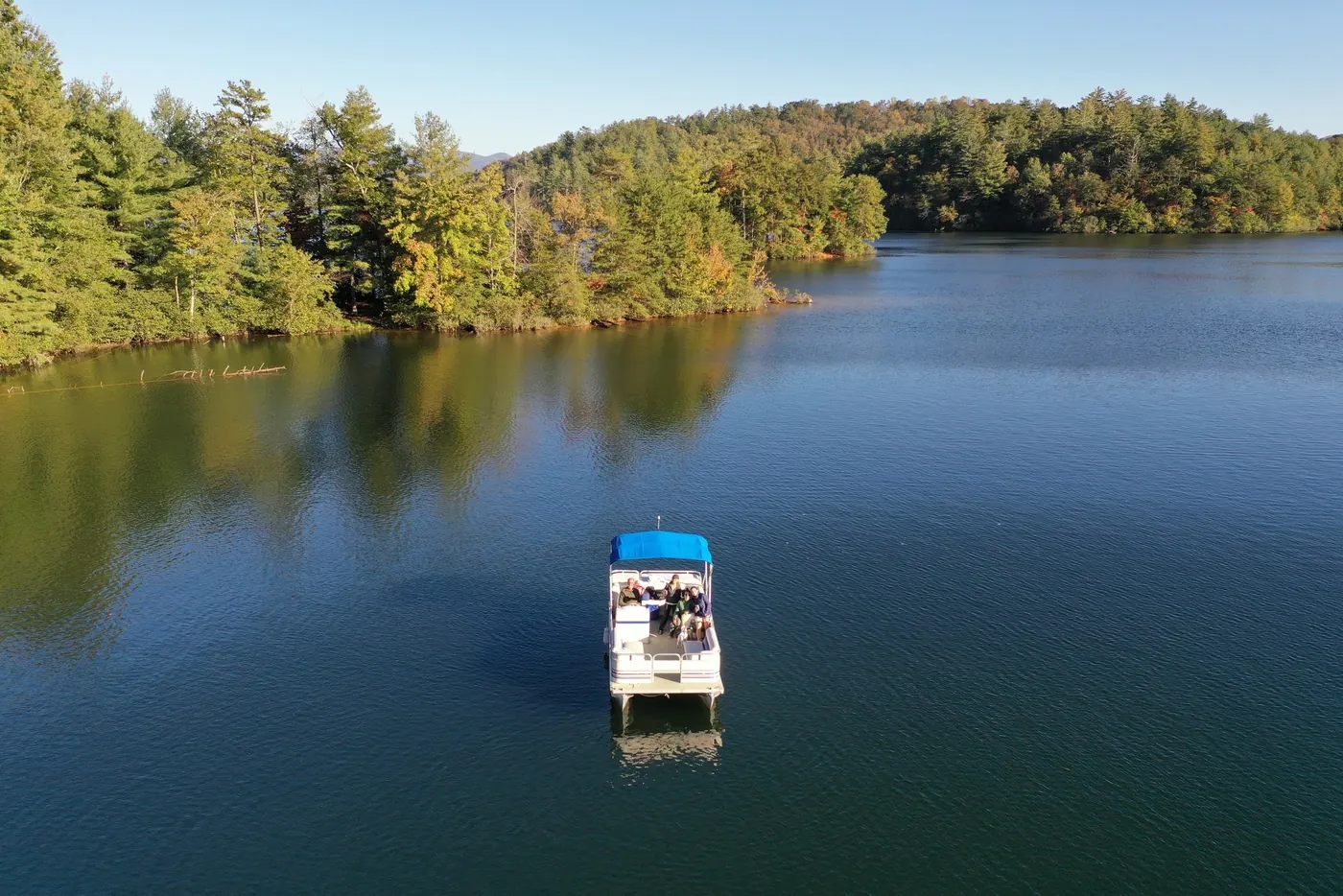 A pontoon boat crossing a quiet mountain lake, seen from above