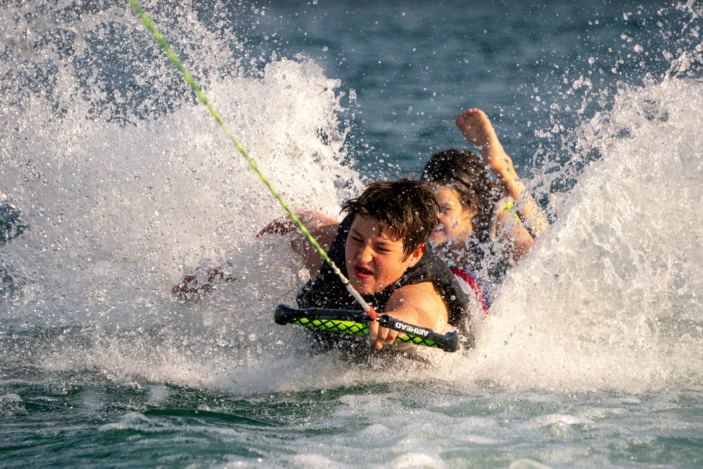 Two kids laughing on a tube pulled behind a boat